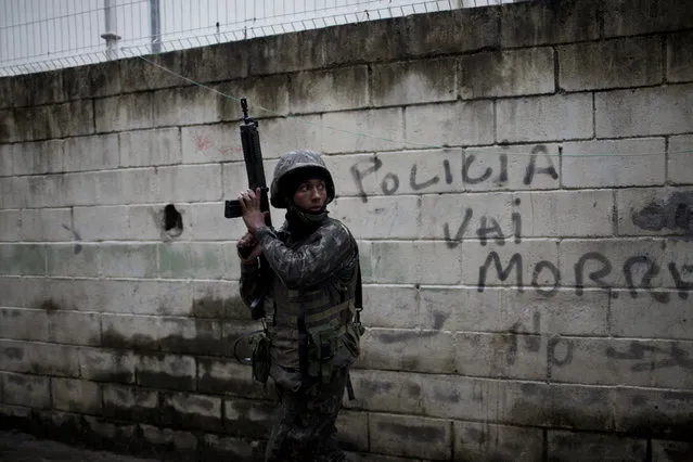 In this Monday, August 21, 2017 photo, a soldier takes position next to a wall spray painted with the Portuguese message: “Police will die” in the Jacarezinho slum during a security operation, in Rio de Janeiro, Brazil. Thousands of soldiers and police are occupying a series of slum communities in northern Rio de Janeiro as part of efforts to combat a spike in violence. (Photo by Silvia Izquierdo/AP Photo)