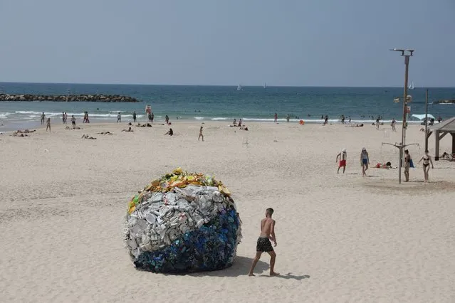A person looks at an art installation created by Israeli artist Tal Tenne Czaczkes of a large beach ball made of plastic waste collected on the beaches is on display at Gordon beach in Tel Aviv, Israel, 10 August 2022. The artwork is on display as part of an initiative by the Tel Aviv municipality to raise people's awareness for protecting the environment. (Photo by Abir Sultan/EPA/EFE)