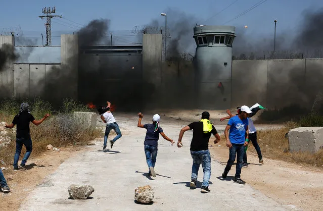 Palestinian youths burn tires and throw stones towards an Israeli military post following the Friday prayer on July 29, 2016 near Qalandia, which is located next to Israel's controversial separation barrier, between the West Bank town of Ramallah and East Jerusalem, three days after Palestinian homes were destroyed by Israeli authorities. On July 26, 2016, Israeli authorities demolished a dozen Palestinian homes in Qalandia, according to Palestinian sources. Witnesses added that shortly after midnight, a convoy of dozens of military vehicles and Israeli bulldozers stormed the area, before demolishing 11 houses. (Photo by Abbas Momani/AFP Photo)