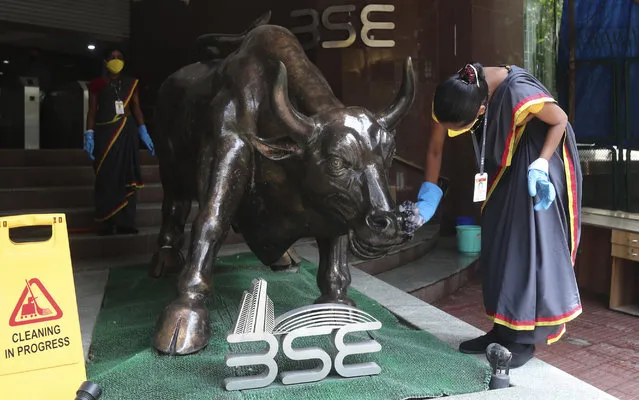 A woman cleans a bronze statue of a bull outside the Bombay Stock Exchange (BSE) in Mumbai, India, Friday, June 12, 2020. Asian shares were moderately lower Friday after an overnight rout on Wall Street as investors were spooked by reports of rising coronavirus cases in the U.S. (Photo by Rafiq Maqbool/AP Photo)