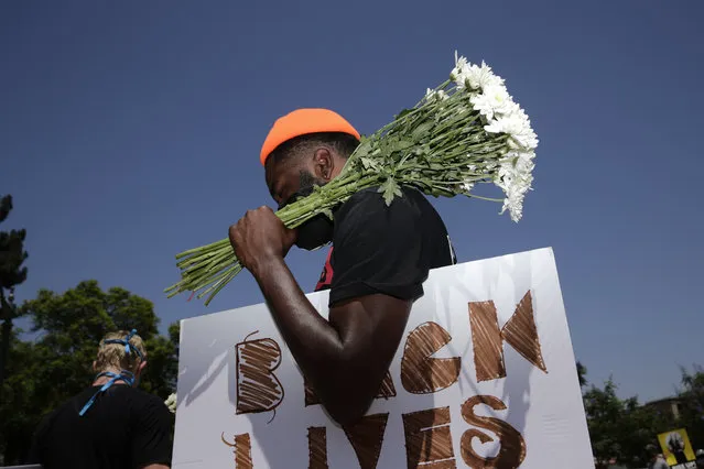 Holding flowers and a sign, Blair Toles, 30, attends rally in Los Angeles, on Black Strike Day, Monday, July 20, 2020. Thousands across the country walked off the job to protest systemic racism and economic inequality that has worsened during the coronavirus pandemic. (Photo by Jae C. Hong/AP Photo)