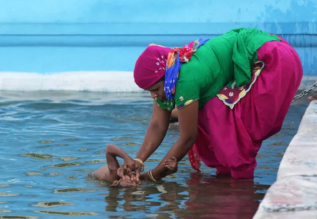 An Indian woman pinches the nose of her child to avoid water as she helps her take a holy dip in the sacred pond of the Golden Temple, the holiest of Sikh shrines on the occasion to mark the 412th first installation anniversary of Sri Guru Granth Sahib, the holy book of Sikhs in Amritsar, India, 02 September 2016. Guru Arjan Dev, the fifth Sikh Guru, installed Guru Granth Sahib for the first time at the Golden Temple in the year 1604. The day is celebrated with religious sentiments and respect by the devotees. (Photo by Raminder Pal Singh/EPA)