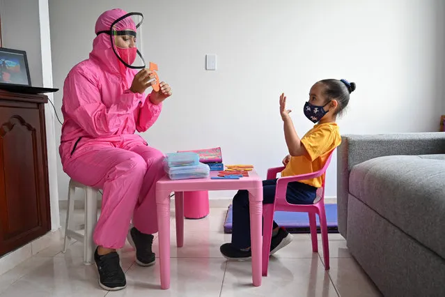 A teacher wearing a biosecurity suit as a preventive measure against the spread of the novel coronavirus, COVID-19, gives a class to a girl at home in Cali, Colombia, on August 4, 2020. The “teacher at home” modality implemented by a local kindergarten seeks to help children keep in touch with teachers and reduce the emotional impact due to isolation during the pandemic. (Photo by Luis Robayo/AFP Photo)
