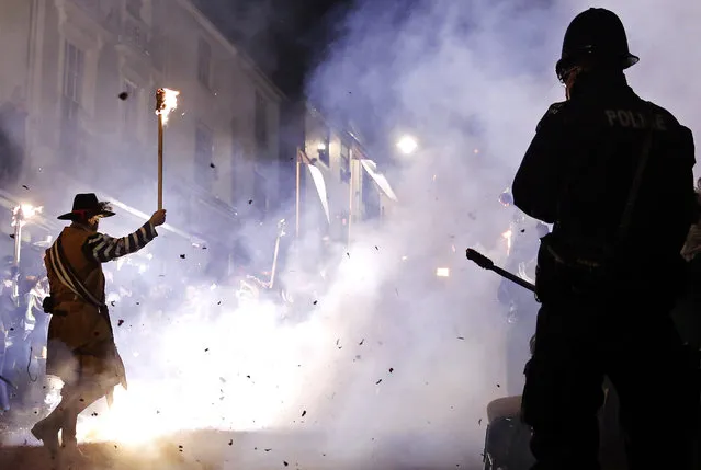 A police watches as participants in costumes hold burning torches during in one of a series of processions during Bonfire night celebrations in Lewes, southern England November 5, 2014. (Photo by Luke MacGregor/Reuters)