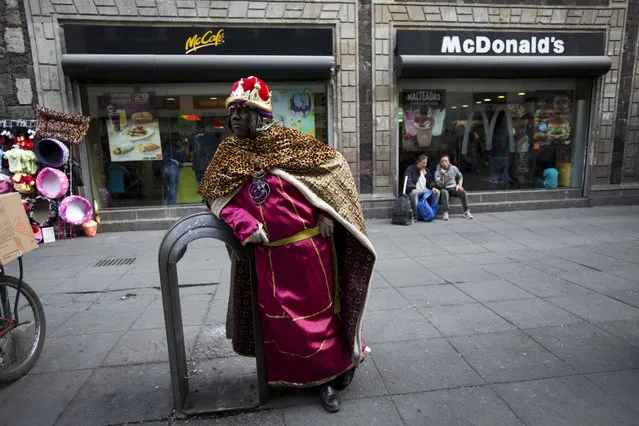 Performance artist David Antonio Lopez De La Fuente Campos, dressed as one of the Three Kings, waits for families wanting to pose for souvenir photos on the eve of the Epiphany, in the historic center of Mexico City, Friday, January 5, 2018. In Mexico, it is customary for people to give gifts on Three Kings Day also known as the Epiphany, commemorated on Jan. 6. According to Christian tradition, Jan. 6 marks the arrival of three wise men bearing gifts for the baby Jesus. (Photo by Rebecca Blackwell/AP Photo)