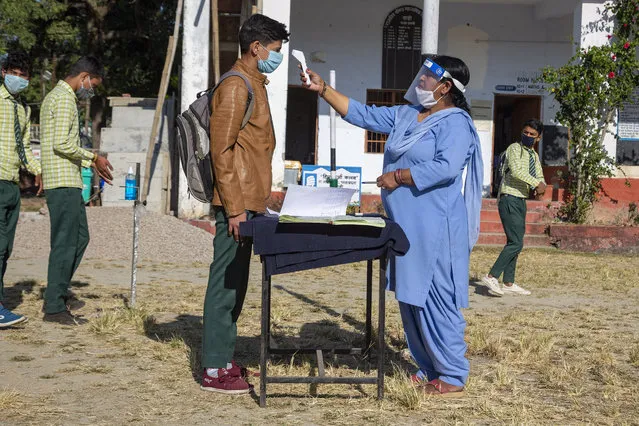 A staff member tests the temperature of students before allowing them into classrooms, as a precautionary measure against the coronavirus, at the Government Senior Secondary School in Dari, near Dharmsala, India, Friday, November 6, 2020. (Photo by Ashwini Bhatia/AP Photo)