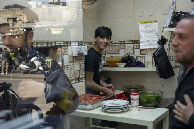 Mohammed Zuad Khaman, center, prepares kebabs at his family's cafe in one of Baghdad's poorer neighborhoods along King Ghazi Street on Monday, February 27, 2023. Khaman is a talented footballer, but he says he cannot get an opportunity to play in any of Baghdad's amateur clubs because he does not have any “in” with the militia-related gangs that control sports teams in the city. (Photo by Jerome Delay/AP Photo)