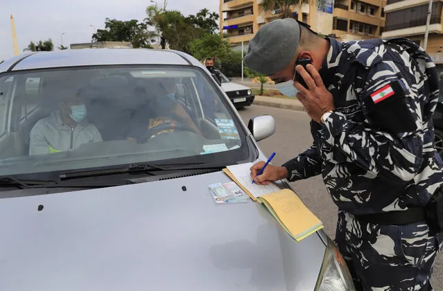 A Lebanese policeman writes a ticket for a car that violated the odd or even number plates car bans, as the country began a two-week lockdown to limit the spread of coronavirus that killed dozens of people over the past days, in Beirut, Lebanon, Saturday, November 14, 2020. The lockdown comes after the number cases increased sharply in recent weeks around Lebanon straining the country's medical sector where intensive care units are almost full. (Photo by Hussein Malla/AP Photo)