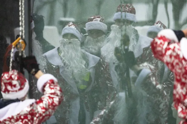 Russian emergency rescue workers dressed as Ded Morozes (Santa Claus, or Father Frost) reflect in a window of a children hospital after scaling the wall to greet children to mark the upcoming New Year celebrations, in Moscow, Russia, Friday, December 25, 2020. Russia, which has so far registered more than 2.9 million confirmed cases of the virus and over 52,000 deaths in the pandemic, has been swept by a rapid resurgence of the outbreak this fall, with numbers of infections and deaths significantly exceeding those reported in the spring. Usually, performers come into children's rooms, but this year because of the virus-related restrictions, the artists had to perform outside of the hospital at a significant distance. (Photo by Pavel Golovkin/AP Photo)