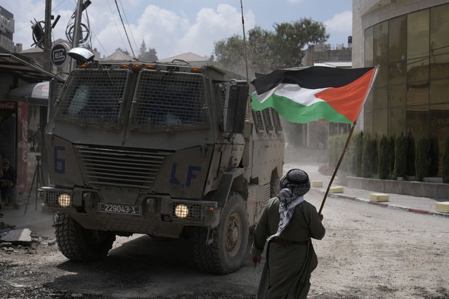A man waves a Palestinian flag as an Israeli armoured vehicle moves on a street during a military operation in the West Bank refugee camp of Nur Shams, Tulkarem, Thursday, August 29, 2024. (Photo by Majdi Mohammed/AP Photo)