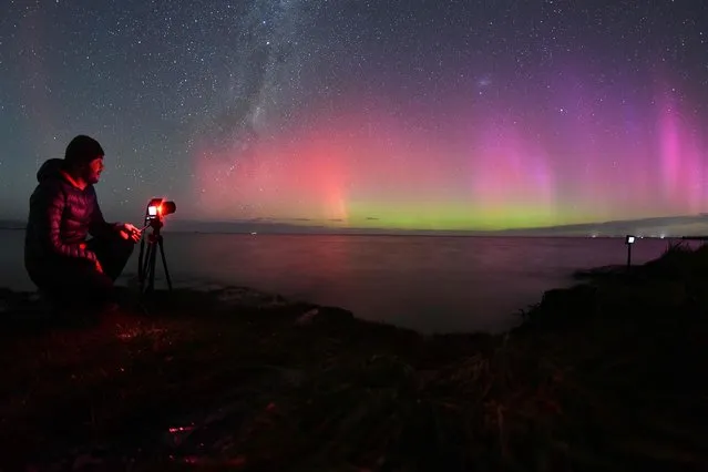 A photographer takes pictures of the Aurora Australis, also known as the Southern Lights, as it glows on the horizon over waters of Lake Ellesmere on the outskirts of Christchurch on April 24, 2023. (Photo by Sanka Vidanagama/AFP Photo)
