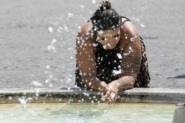 A woman leans by the Lions fountain in Rome, Tuesday, July 18, 2023. Tourist flock to the eternal city while scorching temperatures grip central Italy with Rome at the top of the red alert list as one of the hottest cities in the country. (Photo by Gregorio Borgia/AP Photo)