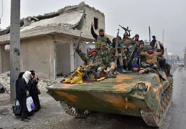 Syrian pro-government forces sit on a military vehicle driving past residents fleeing the eastern part of Aleppo and gathering in Masaken Hanano, a former rebel-held district which was retaken by the regime forces last week, on November 30, 2016. More than 50,000 Syrians have joined a growing exodus of terrified civilians from the besieged rebel-held east of Aleppo, the Syrian Observatory for Human Rights monitor said, as the UN Security Council was set for emergency talks on fighting in the city. Regime forces and allied fighters now fully control the city's northeast and pressed their offensive on November 30 on Aleppo's southeastern edges, advancing in the Sheikh Saeed district, according to state news agency SANA. (Photo by George Ourfalian/AFP Photo)