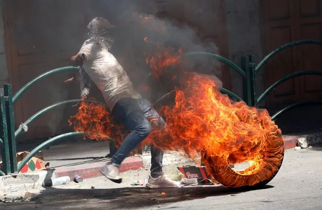 A Palestinian demonstrator kicks a burning tire, during clashes in the West Bank city of Hebron, 14 May 2021. Clashes continue over the forced eviction of six Palestinian families from their homes in Sheikh Jarrah neighborhood in favor of Jewish families who claimed they used to live in the houses before fleeing in the 1948 war that led to the creation of Israel. In response to days of violent confrontations between Israeli security forces and Palestinians in Jerusalem, various Palestinian militants factions in Gaza launched rocket attacks since 10 May that killed at least seven Israelis to date. According to the Palestinian Ministry of Health, 119 Palestinians, including 31 children, were killed as a result of the ongoing Israeli airstrikes on the Gaza Strip. Hamas confirmed the death of Bassem Issa, its Gaza City commander, during an airstrike. (Photo by Abed Al Hashlamoun/EPA/EFE)