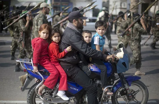 A Palestinian man rides a motorcycle with his children past masked militants of Ezzedine al-Qassam Brigades, Hamas's armed wing, as they parade in Jabalia refugee camp, northern Gaza Strip, on November 14, 2013, during an anti-Israel march as part of the celebrations marking the first anniversary of what Israel named the “Pillar of Defence” Operation. (Photo by Mohammed Abed/AFP Photo)