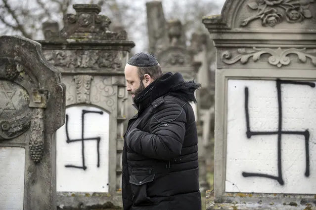 A member of the Jewish community walks among defaced gravestones at the Jewish cemetery of Herrlisheim, near Strasbourg, eastern France, Friday, December 14, 2018. 37 gravestones and a monument for Holocaust victims have been tagged with anti-Semitic graffiti. The graffiti that include Nazi symbols were discovered on Tuesday, hours before a gunman sprayed gunfire near the Christmas market of Strasbourg. (Photo by Jean-Francois Badias/AP Photo)