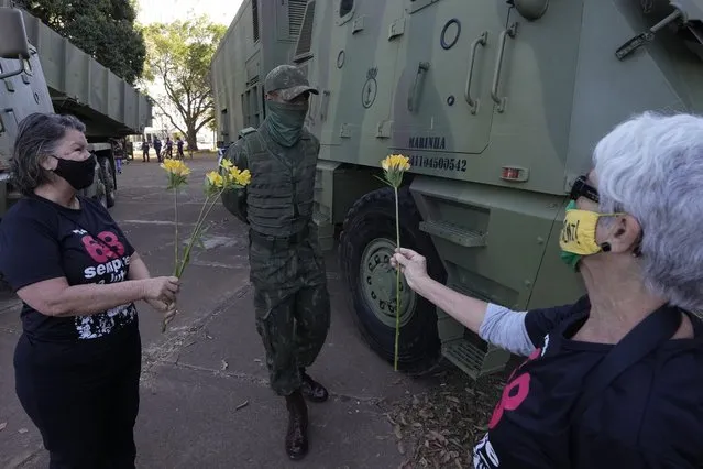 Women offer flowers to a soldier in a show of opposition to Brazilian President Jair Bolsonaro after a military convoy passed Planalto presidential palace and parked outside the Navy headquarters in Brasilia, Brazil, Tuesday, August 10, 2021. (Photo by Eraldo Peres/AP Photo)