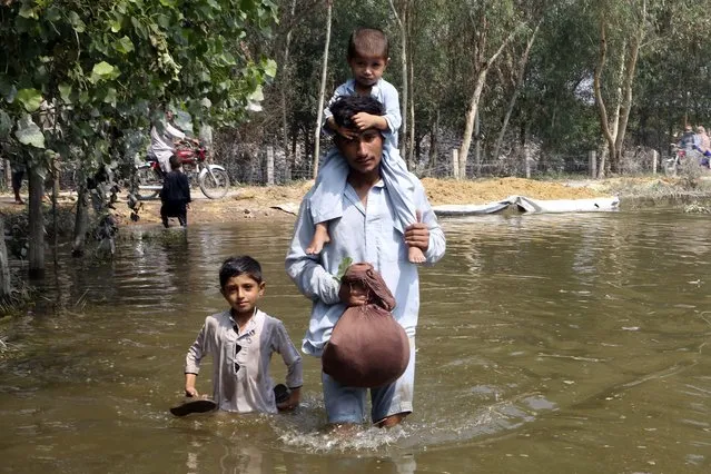 A man carries his son as he wades through floodwaters in Charsadda, Pakistan, Thursday, September 1, 2022. Pakistani health officials on Thursday reported an outbreak of waterborne diseases in areas hit by recent record-breaking flooding, as authorities stepped up efforts to ensure the provision of clean drinking water to hundreds of thousands of people who lost their homes in the disaster. (Photo by Mohammad Sajjad/AP Photo)