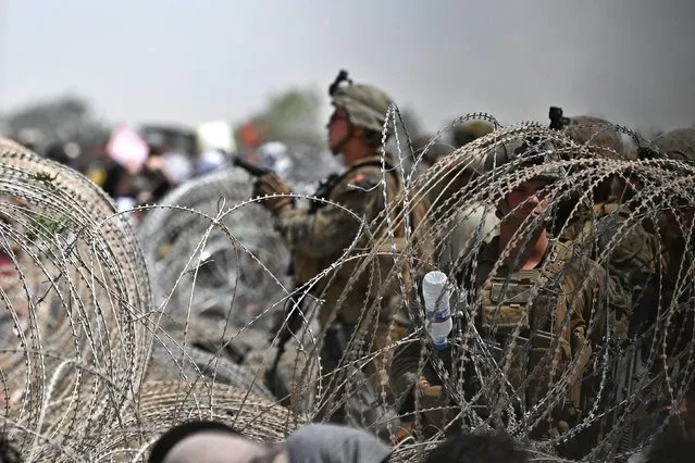 US soldierstand guard behind barbed wire as Afghans gather on a roadside near the military part of the airport in Kabul on August 20, 2021, hoping to flee from the country after the Taliban's military takeover of Afghanistan. (Photo by Wakil Kohsar/AFP Photo)