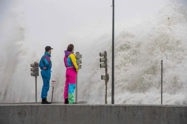People watch waves crash over the sea wall in Revere, Massachusetts on January 13, 2024. The Massachusetts Emergency Management Agency is reminding residents of the possibility of flooding in low-lying areas and streets as a third storm in a week batters the state. (Photo by Joseph Prezioso/AFP Photo)