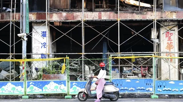A woman stops to look at the burnt building in Kaohsiung in southern Taiwan on Friday, October 15, 2021. Dozens were killed and dozens more injured after a fire broke out early Thursday in a decades-old mixed commercial and residential building in the Taiwanese port city of Kaohsiung, officials said. (Photo by Huizhong Wu/AP Photo)