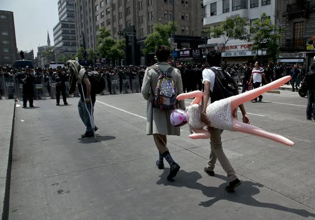 A demonstrator carries and inflatable doll as police blocks the street to prevent demonstrators marking Teacher's Day from approaching the Zocalo plaza in Mexico City, Friday, May 15, 2015. Demonstrators protested against the education reform and the governments' handling of the disappearance of 43 rural teachers' college students in southern Mexico last year. (Photo by Marco Ugarte/AP Photo)