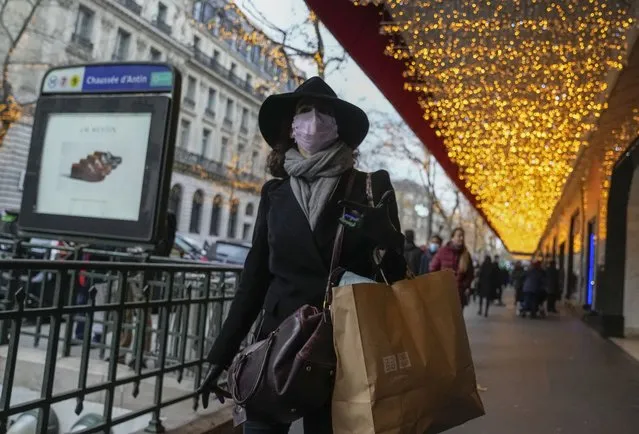 A woman wearing face mask to protect against COVID-19 walks with a shopping bag along a shopping center in Paris, Friday, December 17, 2021. France's government is desperately trying to avoid a new lockdown or stricter measures that would hurt the economy and cloud President Emmanuel Macron's expected campaign for the April presidential election. (Photo by Michel Euler/AP Photo)