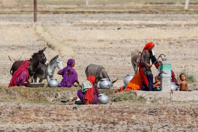 Women with children and their pet donkeys gather for washing and to fetch water at a handpump during a hot summer day on the outskirts of Larkana, Pakistan on May 23, 2024. (Photo by Akhtar Soomro/Reuters)