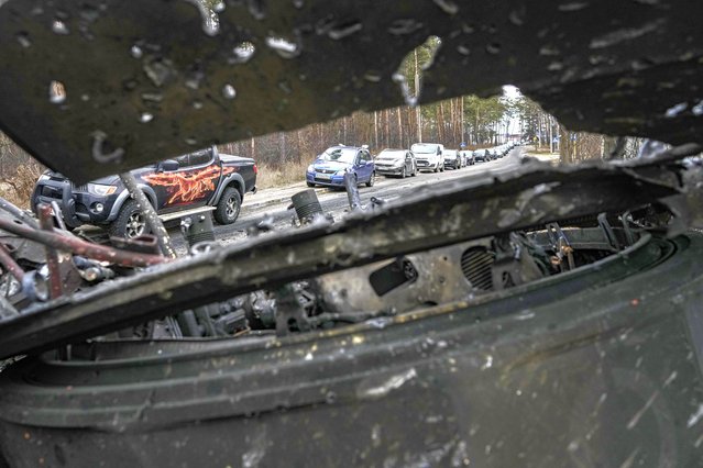 Cars drive past a destroyed Russian tank as a convoy of vehicles evacuating civilians leaves Irpin, on the outskirts of Kyiv, Ukraine, Wednesday, March 9, 2022. (Photo by Vadim Ghirda/AP Photo)