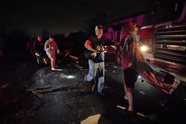 Melodie Maher stands in front of a fire truck as her son, Claude Maher, along with firefighters, rescue her dog from her heavily damaged home after a tornado struck the area in Arabi, La., Tuesday, March 22, 2022. A tornado tore through parts of New Orleans and its suburbs Tuesday night, ripping down power lines and scattering debris in a part of the city that had been heavily damaged by Hurricane Katrina 17 years ago. (Photo by Gerald Herbert/AP Photo)