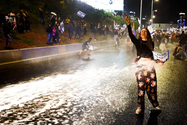 A woman gestures while being sprayed by a water canyon during a demonstration against Israeli Prime Minister Benjamin Netanyahu and his nationalist coalition government's plan for judicial overhaul, in Tel Aviv, Israel on April 1, 2023. (Photo by Ronen Zvulun/Reuters)