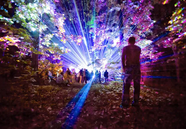 A man watches from a distance as youngsters dance during a music and laser show, in a forest outside Bucharest, Romania, early Saturday, May 21, 2016. People attended in large numbers a display of laser lighting and music that lasted until the morning hours. (Photo by Vadim Ghirda/AP Photo)
