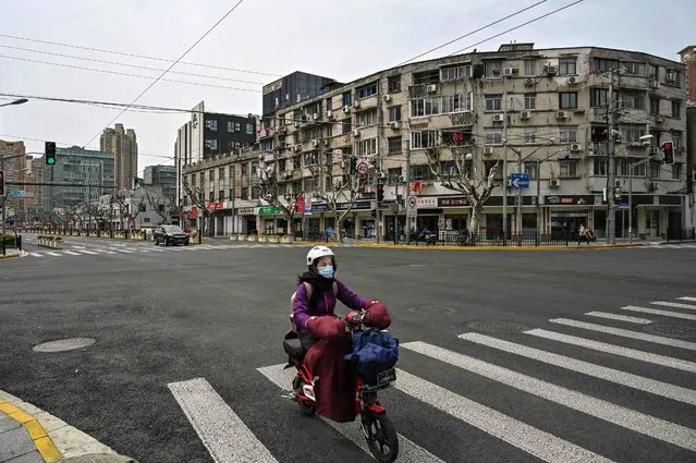A woman drives a scooter down a quiet street in Yangpu distric, in Shanghai on March 28, 2022. Millions of people in China's financial hub were confined to their homes on March 28 as the eastern half of Shanghai went into lockdown to curb the nation's biggest Covid outbreak. (Photo by Hector Retamal/AFP Photo)