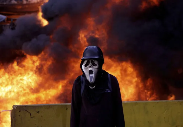 A protester wearing a GhostFace mask stands in front of a truck expropriated and set aflame by protesters during clashes with security forces in Caracas, Venezuela, Saturday, May 27, 2017. Security forces used tear gas and water to disperse protesters who were blocking a highway during a march to cite the decade old decision of the late Hugo Chavez to not renew the network license for Radio Caracas Television (RCTV) network. Chavez had refused to renew RCTV's broadcast license, accusing it of “subversive” activities and of backing a 2002 coup against him. (Photo by Fernando Llano/AP Photo)