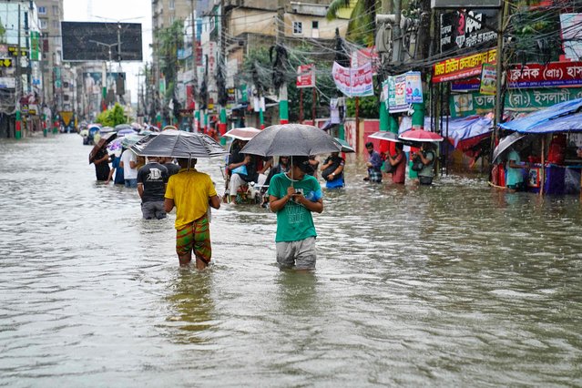 People carrying umbrellas, wade through a flooded street amid rainfall in Feni on August 22, 2024. (Photo by AFP Photo/Stringer)