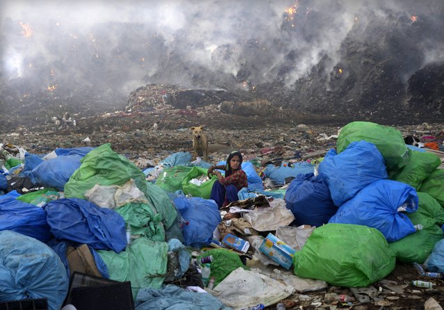 A ragpicker woman segregates items sitting at the edge during a fire at the Bhalswa landfill in New Delhi, India, Wednesday, April 27, 2022. The landfill that covers an area bigger than 50 football fields, with a pile taller than a 17-story building caught fire on Tuesday evening, turning into a smoldering heap that blazed well into the night. India's capital, which like the rest of South Asia is in the midst of a record-shattering heat wave, was left enveloped in thick acrid smoke. (Photo by Manish Swarup/AP Photo)