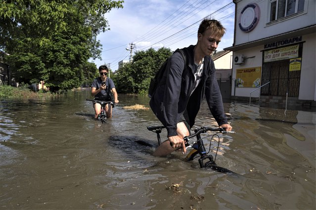 Local residents try to ride their bikes along a flooded road after the Kakhovka dam blew overnight, in Kherson, Ukraine, Tuesday, June 6, 2023. Ukraine on Tuesday accused Russian forces of blowing up a major dam and hydroelectric power station in a part of southern Ukraine that Russia controls, risking environmental disaster. (Photo by Evgeniy Maloletka/AP Photo)