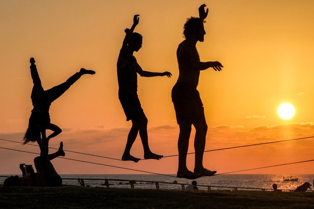 People walk on a tightrope along the Mediterranean sea waterfront in Tel Aviv at sunset on October 10, 2024. (Photo by Ahmad Gharabli/AFP Photo)