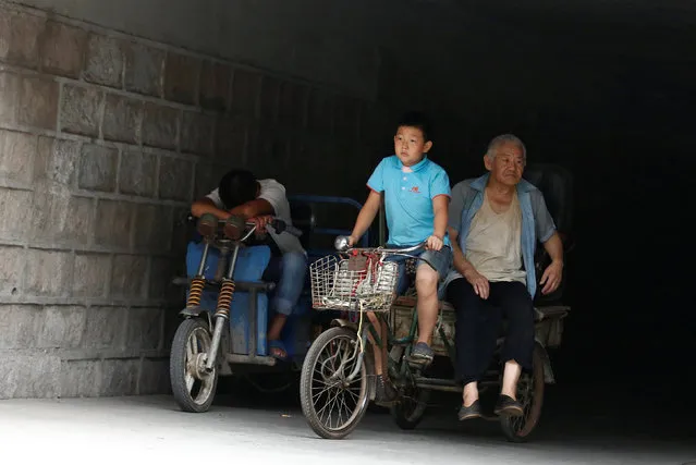 A boy and a man ride a trike past a man resting on the handle bar of his vehicle in Beijing, China July 15, 2016. (Photo by Thomas Peter/Reuters)