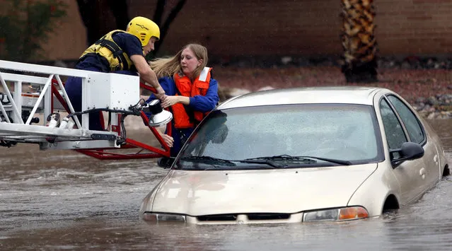Tucson Fire Department personnel use a ladder truck to rescue a woman from a car stranded in rising flood waters in east Tucson, Ariz., Tuesday, August 19, 2014. (Photo by Kelly Presnell/AP Photo/Arizona Daily Star)