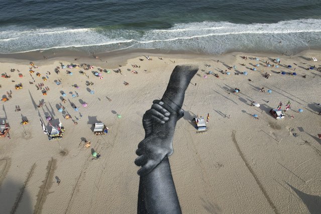 A land-art fresco made with biodegradable paint of charcoal, chalk, water and milk proteins, by French-Swiss artist Saype, covers Copacabana beach as part of the artist's worldwide project titled Beyond Walls in Rio de Janeiro, Brazil, Friday, July 15, 2022. The artist said he is creating a symbolic human chain around the world with the aim of promoting togetherness, kindness and openness to the world. (Photo by Silvia Izquierdo/AP Photo)