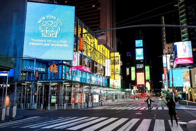 People walk in Times Square, Manhattan while some screens are seen illuminated in blue as part of the “Light It Blue” initiative to honor healthcare workers during the outbreak of the coronavirus disease (COVID-19) in New York City, New York, U.S., April 9, 2020. (Photo by Eduardo Munoz/Reuters)