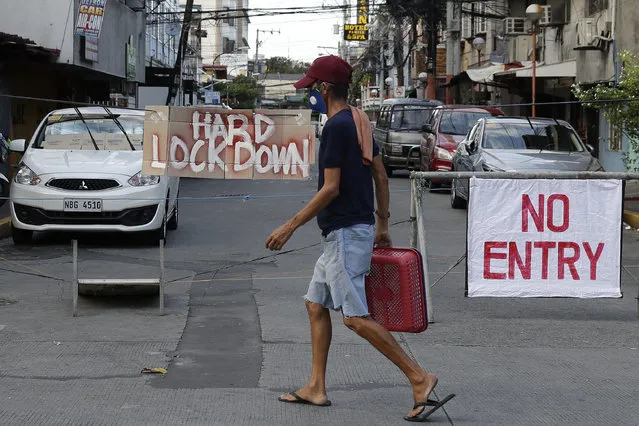 A man wearing a protective mask passes by a sign placed in the middle of a road during a stricter community quarantine to prevent the spread of the new coronavirus in Manila, Philippines, Friday, April 24, 2020. Philippine President Rodrigo Duterte angrily threatened to declare martial law after accusing communist rebels of killing two soldiers who were escorting food and cash deliveries during a coronavirus quarantine. (Photo by Aaron Favila/AP Photo)