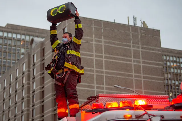 A member of the New York City Fire Department stands on top of a firetruck holding up a speaker playing “New York, New York” by Frank Sinatra in honor of medical staff and essential workers outside of NYU Langone Health hospital amid the coronavirus pandemic on April 30, 2020 in New York City, United States. COVID-19 has spread to most countries around the world, claiming over 230,000 lives with over 3.2 million cases. (Photo by Alexi Rosenfeld/Getty Images)