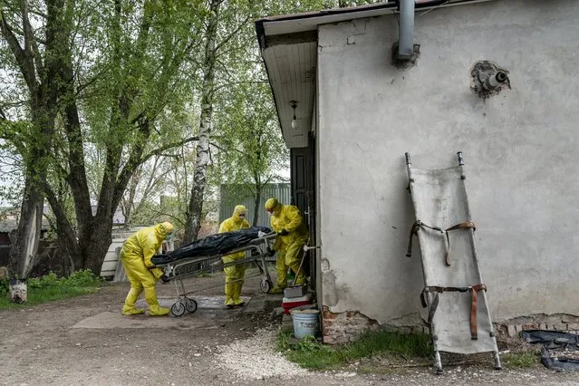 In this photo taken on Thursday, April 30, 2020, pathologists wearing special suits to protect against coronavirus, transport the body of a man who died of coronavirus, at the doors of the morgue in Ternopil, Ukraine. (Photo by Evgeniy Maloletka/AP Photo)