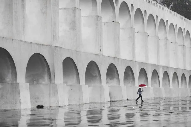 A man with an umbrella walks past the Carioca Aqueduct, also know as Arcos da Lapa, in Rio de Janeiro, Brazil, Thursday, September 29, 2022. (Photo by Matias Delacroix/AP Photo)