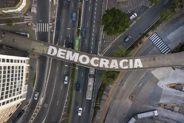 People walk on a pedestrian bridge that has text written on it that reads in Portuguese: “Democracy” in Sao Paulo, Brazil, Wednesday, October 26, 2022. Brazil is set for a presidential run-off election scheduled for Oct. 30. (Photo by Matias Delacroix/AP Photo)
