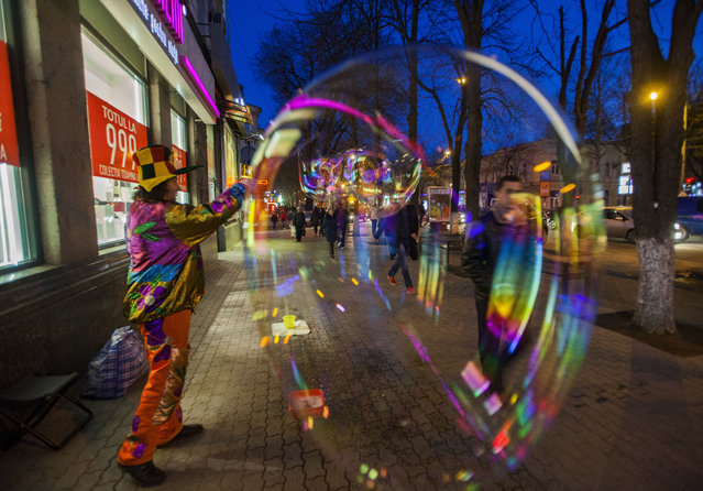 A man dressed as a clown makes huge soap bubbles, as part of Martisor, in downtown Chisinau, Moldova, on 01 March 2016. The Martisor is a traditional souvenir in Moldova and Romania, which is given to loved ones, in the first days of spring. The tradition is to celebrate life after winter. It was previously called “dachia dragobete” – the end of winter. (Photo by Dumitru Doru/EPA)