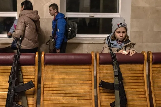 A child stands next to policemen's weapons placed on chairs as she waits for the boarding of an evacuation train heading to Kyiv, at the railway station in Kherson, southern Ukraine, 25 November 2022. Russian troops for the past few days intensified the shelling of Kherson. On its retreat from Kherson, the Russian army destroyed critical infrastructure in the city, including electricity and water supplies. Now the lack of electricity and running water in the town during the winter season has forced many locals to flee Kherson. (Photo by Roman Pilipey/EPA/EFE)