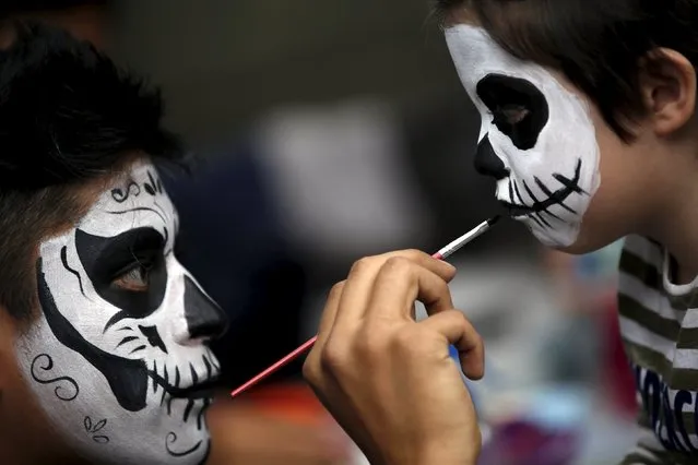 A man with his face painted to look like the popular Mexican figure called "Catrin ", paints a boy's face as they take part in the annual Catrina Fest in Mexico City November 1, 2015. (Photo by Carlos Jasso/Reuters)